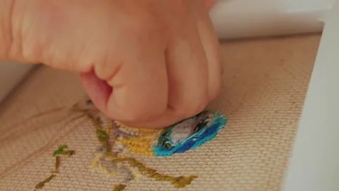 A close-up of a hand embroidering colorful threads onto a textured fabric Stock Footage 312953687