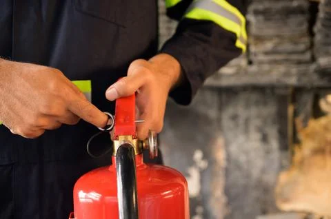 Close up hand Fireman using fire extinguisher fighting. Hand pulling pin of.. Stock Photos