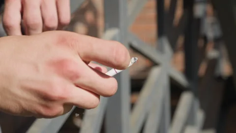 close up hand flicking cigarette while resting on iron railing