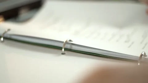 Close-up of a hand flipping through printed script pages in a binder. Focus on Stock Footage 336042586