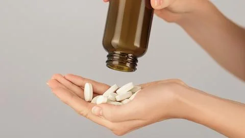 Close-up of a hand full of white tablets being poured from a bottle Stock Photos
