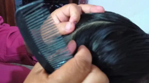 Close-up of a hand gently running a comb through a child's shiny black hair. Stock Footage 321941183