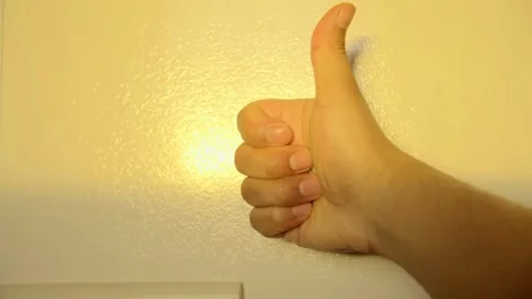 Close-up of a hand giving a thumbs up gesture against a warm background. Vídeo Stock 323390146