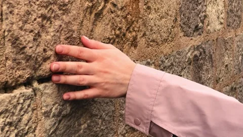 A close-up of a hand gliding smoothly across a rough stone wall, slowly tracing Video stock 334998884