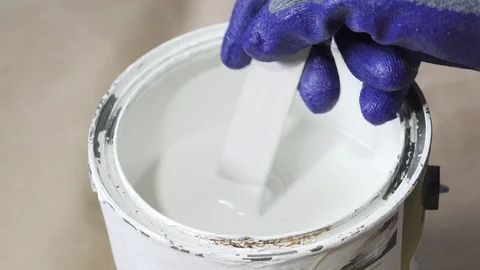 Close up of hand gloved painter mixing white paint with wooden stick. Stock Footage 129139513