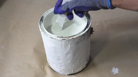 Close up of hand gloved painter mixing white paint with wooden stick. Stock Footage 129139583