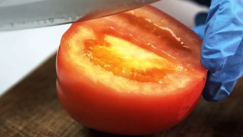 Close-up of hand with gloves knife is cut ripe tomato on wooden board. Stock Footage 82237102