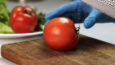 Close-up of hand in gloves with knife is cut ripe tomato. Stock Footage 82358760