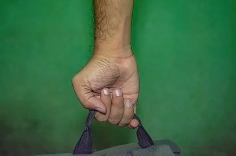 Close up of a hand gripping a backpack strap against a green background, ca.. Stock-Fotos