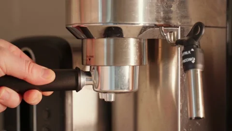 A close-up of a hand-held barista inserting a steel horn portafilter into a Stock Footage 234905211