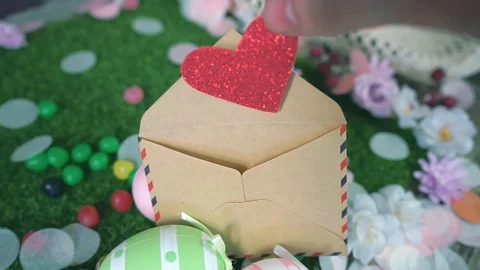 Close-up of hand hides a glitter red heart into a envelope between Easter eggs Stock Footage 101290774