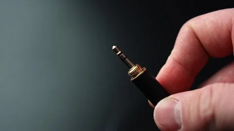 Close-up of a hand holding a 3.5mm audio jack plug with copy space on a dark Stock Footage 329487822