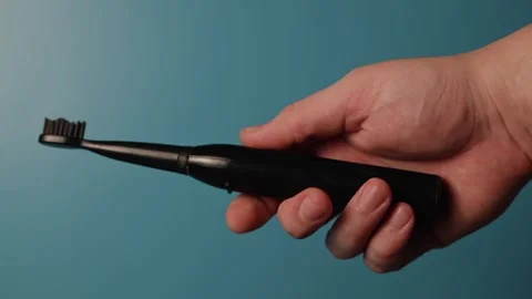 Close up of hand holding and operating a black electric toothbrush Stock Footage 340267873