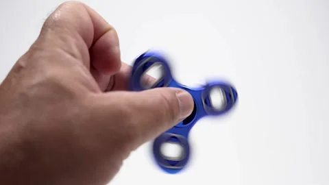 A close-up of a hand holding and spinning a metallic blue fidget spinner. Stock Footage 313053968