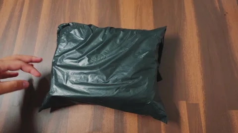 Close-up of Hand Holding Black Plastic Delivery Package on Wooden Floor Stock Footage 333321987