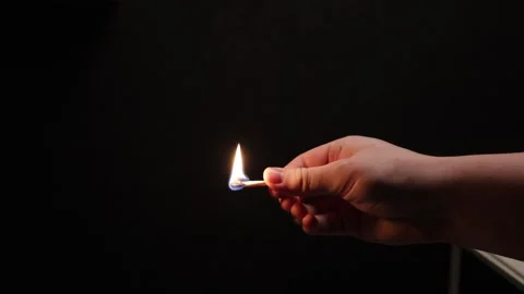 Close-up of a hand holding a burning matchstick against a dark background Stock Footage 339177104