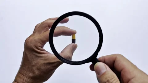 Close-up of a hand holding a capsule under a magnifying glass 库存影片 338364644
