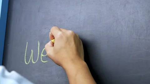Close up of a hand holding a chalk and writing welcome on the blackboard Stock Footage 160814729