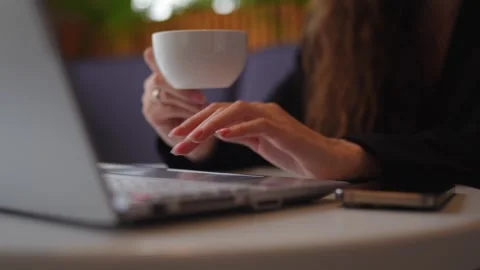 Close-up of a hand holding a coffee cup near a laptop, symbolizing a relaxed wor Stock Footage 292906945