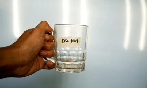 Close up hand holding empty drinking glass with text word drink written on du Foto stock