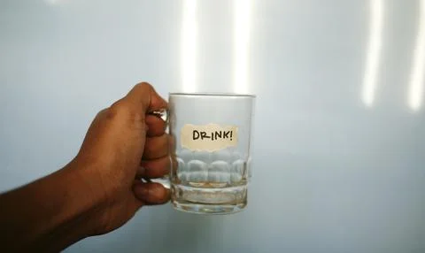 Close up hand holding empty drinking glass with text word drink written on du Foto stock