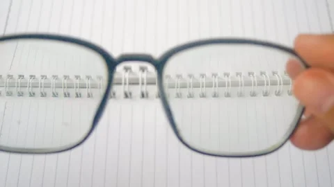Close up of a hand holding eyeglasses in front of an eye chart on a noteboo.. Stock Footage 332914003