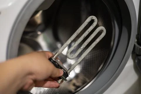 Close-up of a hand holding a heating element covered with limescale. Washing Stock Photos