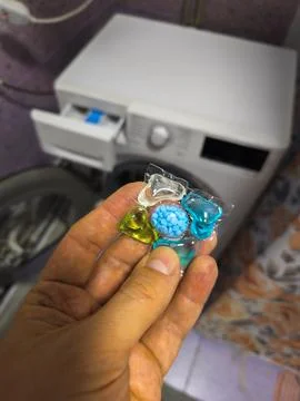 Close-Up of Hand Holding Laundry Detergent Pods Near Washing Machine Stock Photos