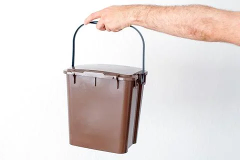 Close-up of a hand holding an open brown organic waste bucket with an eco-f.. 库存照片