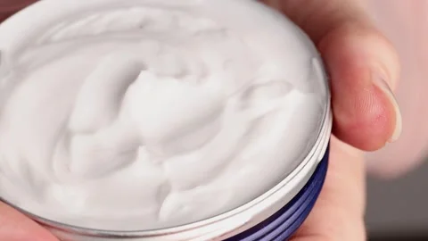 Close-up of a hand holding an open tin with moisturizing cream, smooth white Stock Footage 304679307