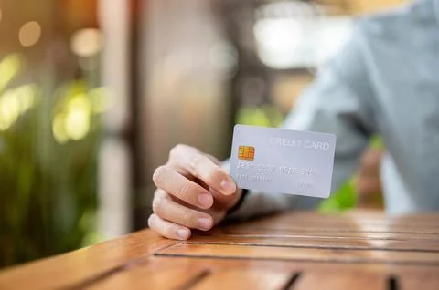 Close up of a hand holding or showing a credit card while sitting at wooden.. Stock Photos