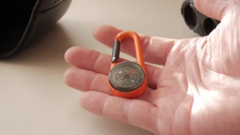 Close-up of hand holding orange compass carabiner for hiking or travel Video stock 308939098