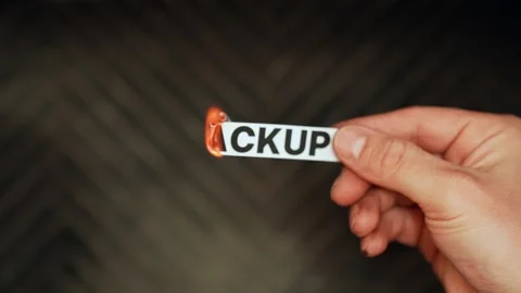 Close-up of a hand holding a paper label reading “BACKUP” as it catches fire Stock Footage 329288149