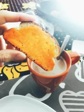Close-Up Of Hand Holding Piece of Bread near Milk Cup Stock Photos