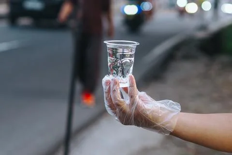 Close up of hand holding plastic cup filled with water, bokeh, giving water.. Stock Photos