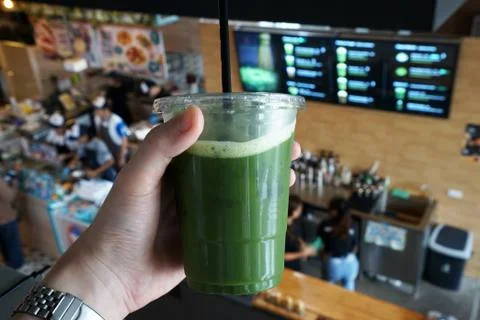Close up Hand holding a plastic take away cup of Iced Matcha green tea Stock Photos