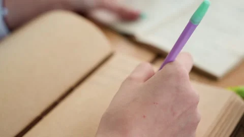 Close up hand holding purple and green pen over open notebook in study setting Stock Footage 345842485