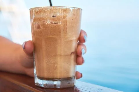 Close-up of a hand holding a refreshing iced coffee frappe near the sea in .. Stock Photos