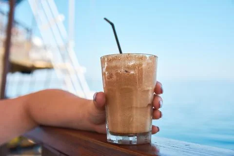 Close-up of a hand holding a refreshing iced frothy coffee drink by the sea Stock Photos