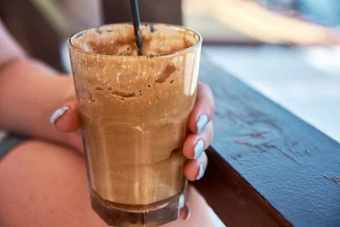 Close-up of a hand holding a refreshing iced coffee frappe in a glass Stock Photos