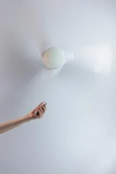 Close-up of hand holding remote control of white ceiling fan. Hand turning on 写真素材