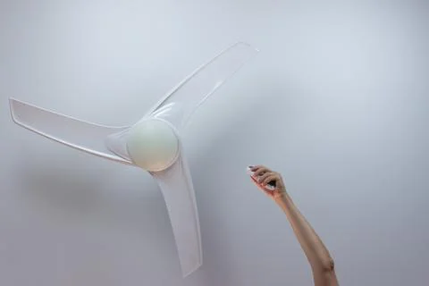 Close-up of hand holding remote control of white ceiling fan. Hand turning on Stock Photos