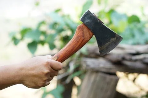 Close up of a hand holding a sharp hatchet with wooden handle near a chopping bl Stock Photos