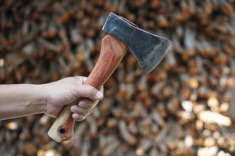Close up of a hand holding a sharp hatchet with a wooden handle against a blurre Stock Photos