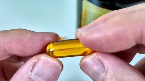 Close-up of a hand holding a single golden omega-3 fish oil dietary supplement Stock Footage 345365668