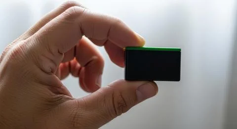 Close up hand holding a small black square object with shallow depth of fie.. 库存插图