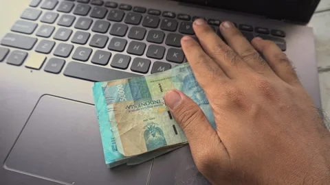 Close up of hand holding a stack of Indonesian rupiah banknotes over laptop.. Stock Footage 345135291