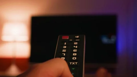 A close-up of a hand holding a TV remote control and changing channels. The TV Stock Footage 335749327