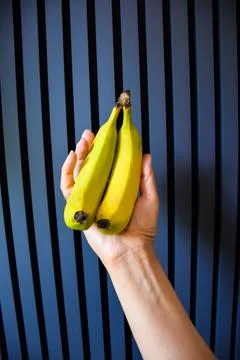 Close up of a hand holding two fresh yellow bananas vertically against Stock Photos