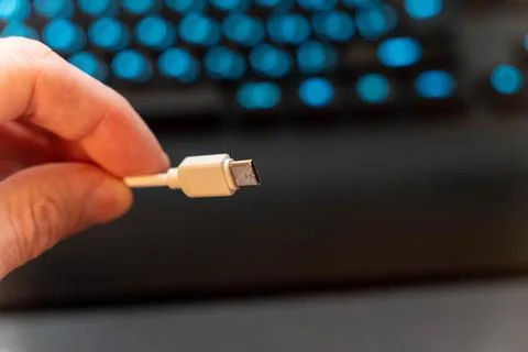 Close-up of a hand holding a white USB cable with a blue keyboard in the ba.. Stock-Fotos